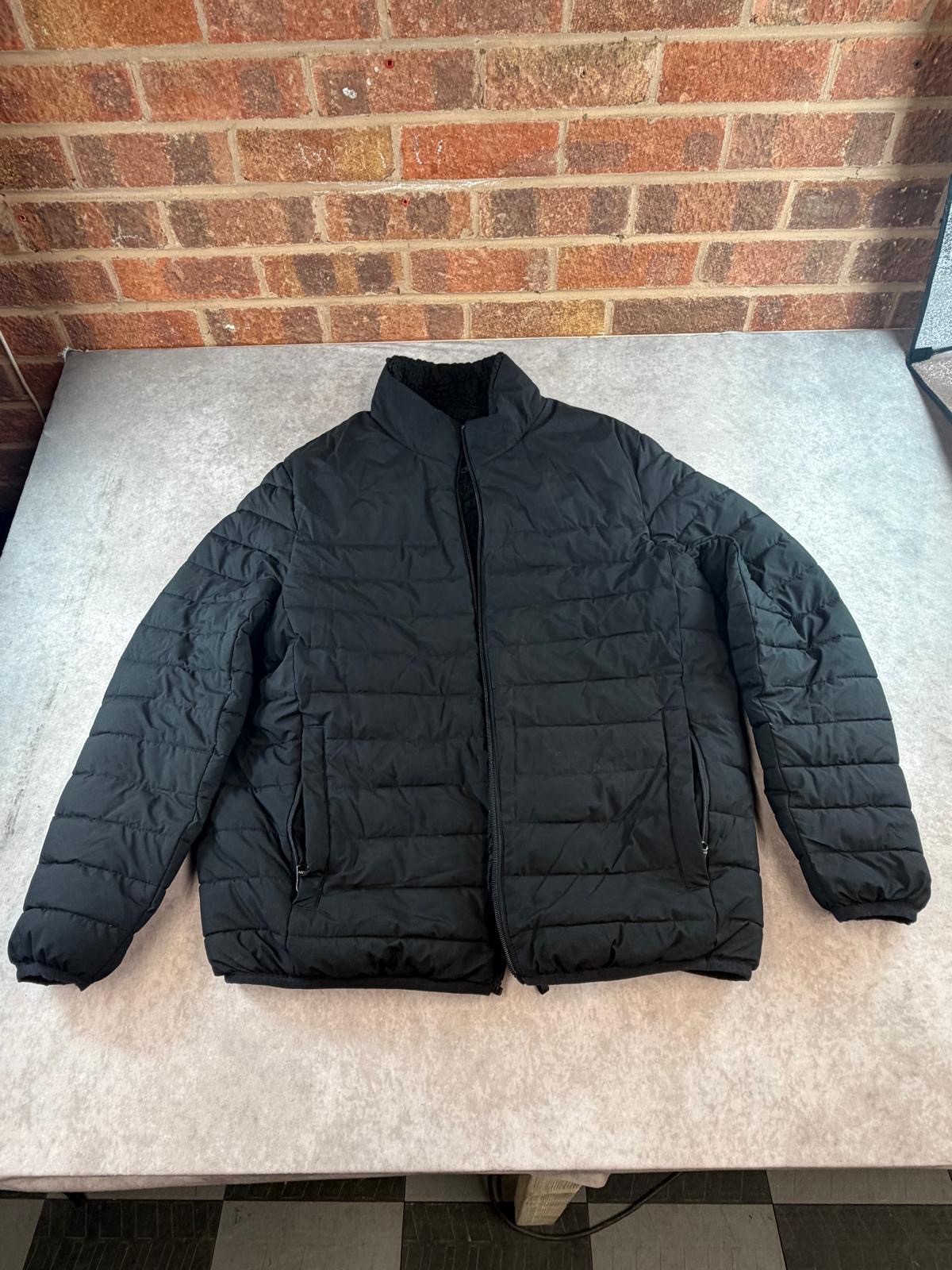 Full front view of the black quilted puffer jacket on a grey surface against a brick wall