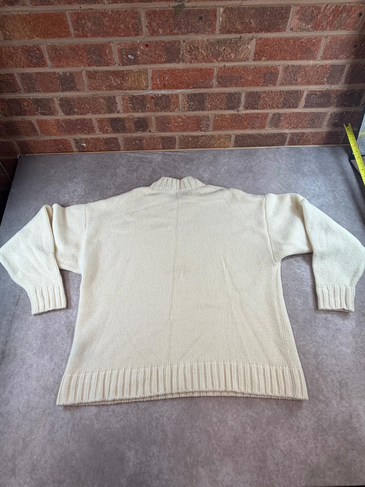 Back view of the cream wool jumper flat on a grey surface against a brick wall